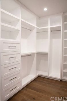 an empty walk in closet with white shelves and drawers