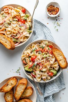 two bowls filled with pasta and vegetables next to garlic bread