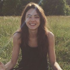 a woman sitting in the grass with her eyes closed and hands out, smiling at the camera