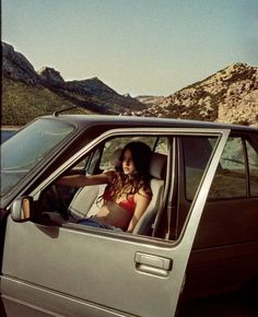 a woman sitting in the passenger seat of a car with mountains in the back ground