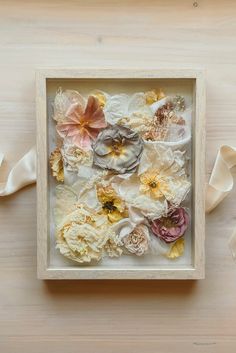 a wooden frame with flowers in it on a table next to some white satin ribbons