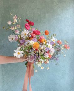 a person holding a bouquet of flowers with pink ribbon around the bottom and white daisies on top