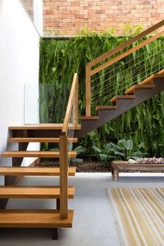 a wooden stair case next to a brick wall with plants growing on it and a bench in the foreground