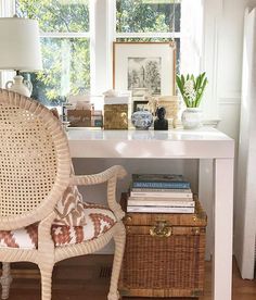 a wicker chair sitting in front of a window next to a table with books