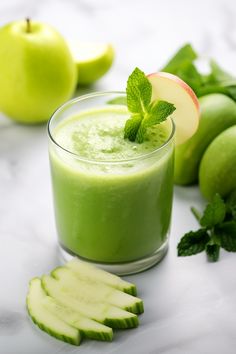 a glass filled with green smoothie next to sliced apples