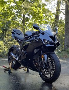 a black motorcycle parked on the side of a road in front of trees and a skateboard