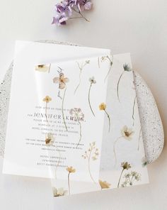 the wedding stationery is laid out on top of each other, with purple flowers in the background