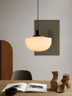 an open book sitting on top of a wooden table next to a vase and lamp