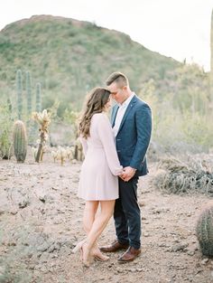 a man and woman standing next to each other in the desert with cactus behind them