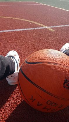 an orange basketball sitting on top of a red court next to someone's feet