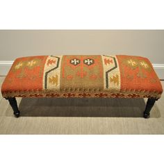 a bench with an orange and beige rug on it's backrest, sitting in front of a wall