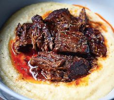 a bowl filled with meat and sauce on top of a white table next to a fork