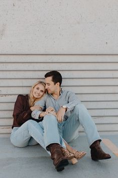 a man and woman sitting on the ground next to each other with their arms around each other