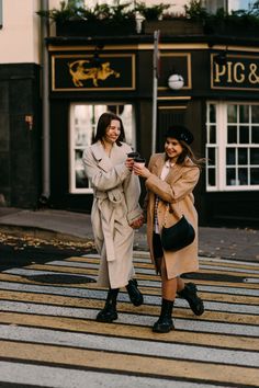 two women are crossing the street and one is holding a cell phone in her hand