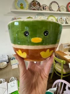 a hand holding up a green bowl with yellow and brown designs on it's face