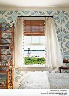 a bedroom with blue and white wallpaper has a large window overlooking the water in front of it