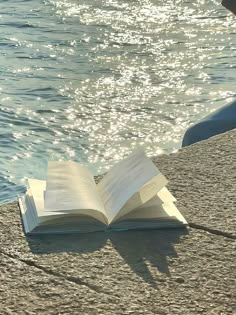 an open book sitting on top of a beach next to the ocean with water in the background