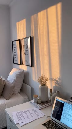 a laptop computer sitting on top of a desk next to a white couch and window