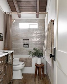 a white toilet sitting next to a bath tub in a bathroom on top of a wooden floor