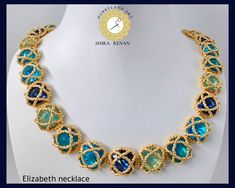 a gold necklace with blue and green stones on it's sides, sitting on a white mannequin