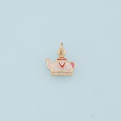 a gold charm with a pink teapot on it's side and a red heart in the middle