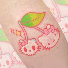 two hello kitty tattoos on the leg of a woman's legs, one is holding a green leaf