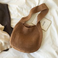 a brown purse sitting on top of a bed next to a white shirt and black pants