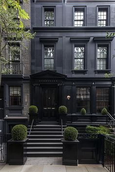 a black building with steps leading up to it and trees in the front garden area