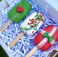 two decorated desserts in a box with strawberries and strawberry on them, one is green and the other is red