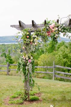 a wooden cross with flowers on it in the middle of a grassy area next to a fence