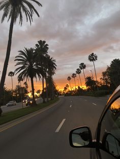 the sun is setting behind palm trees on the side of the road in front of a car