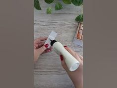 a person holding a white object in their hand on top of a wooden table next to plants