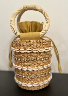 Our Leah Bag is our new favorite mini bag for spring and summer! With shell and stone embellished detail on a simple straw bag with round handles, this handheld adds style and personality to any outfit.  Material: 100% straw, 100% Cotton Lining, Shell and Stone Detail Spot Clean with Damp Cloth Elegant Bucket Bag With Braided Handles For Beach, Elegant Straw Bag With Handles For Beach, Elegant Beach Straw Bag With Handles, Chic Straw Bag With Round Handle For Beach, Chic Top Handle Straw Bag For Beach, Chic Beach Straw Bag With Top Handle, Elegant Straw Bag With Round Handle For Beach, Summer Beach Bags Made Of Shell, Summer Beige Straw Bag With Pearl Handle