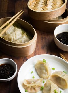 dumplings with sauce and chopsticks sit on a plate next to two bowls