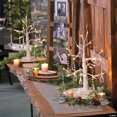 a table topped with candles and trees covered in greenery on top of a wooden table