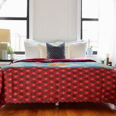 a bed with red and blue bedspread in front of two windows