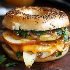 a bagel sandwich with onions, cheese and other toppings on a wooden surface