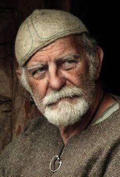 an old man with a white beard wearing a hat and looking off to the side