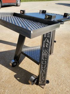 a metal table sitting on top of a parking lot next to a red car in the background