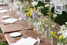 a long wooden table topped with glass vases filled with wildflowers and other flowers