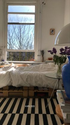 a room with a bed, table and window in it's center area that has black and white stripes on the floor