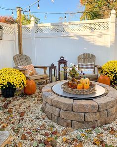 a fire pit surrounded by yellow flowers and pumpkins on the ground in front of a white fence