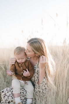 a woman holding a baby in her arms while sitting on the ground with tall grass