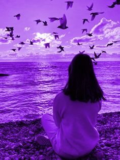 a woman sitting on the beach looking at birds flying in the sky