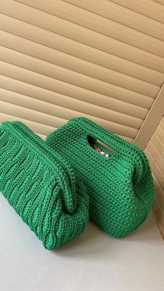 two green knitted purses sitting on top of a white table next to each other