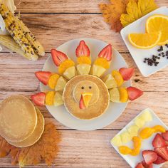 a plate topped with pancakes and fruit next to oranges, strawberries and corn on the cob