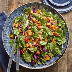 a blue plate topped with spinach salad next to a fork and knife on top of a wooden table