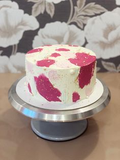 a white and pink cake sitting on top of a metal stand next to a floral wallpaper