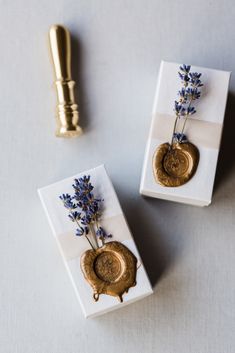 two small vases with flowers on them sitting next to a gold spoon and knife