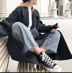 a woman is sitting on a bench and looking at her cell phone while wearing converse sneakers